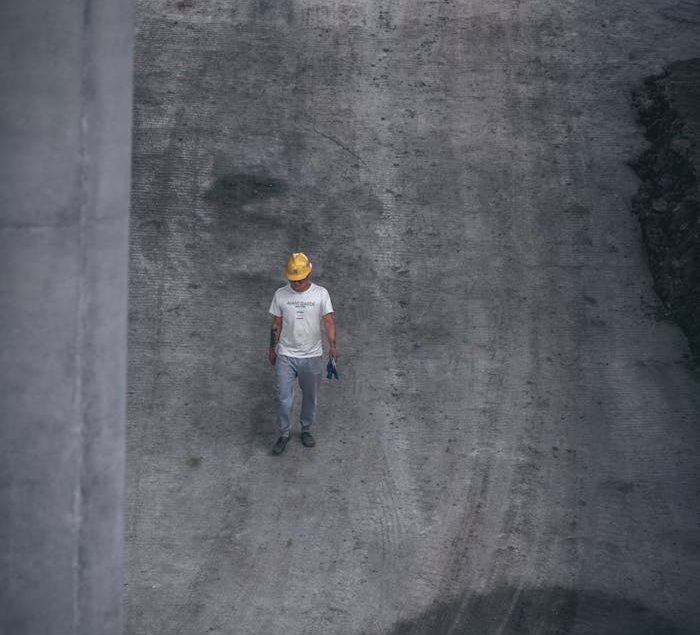 A man in a safety helmet walking on a construction site, viewed from above for a unique perspective.
