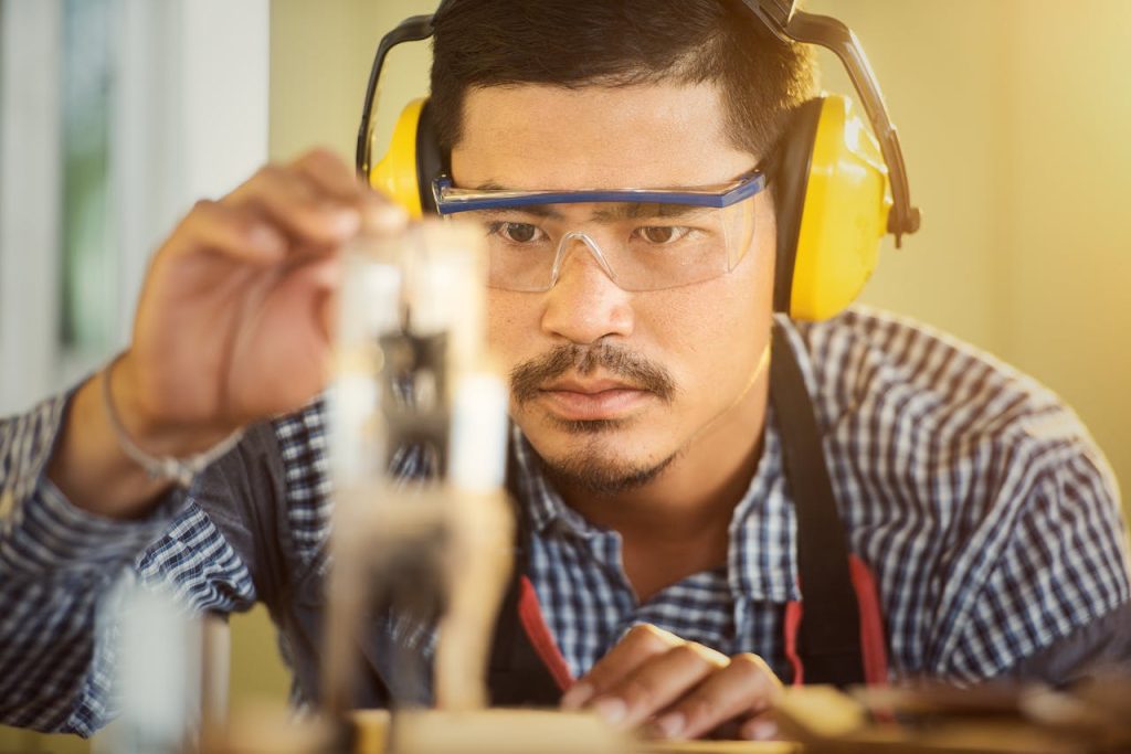 Carpenter wearing protection gear measuring wood in a workshop with great focus and precision.