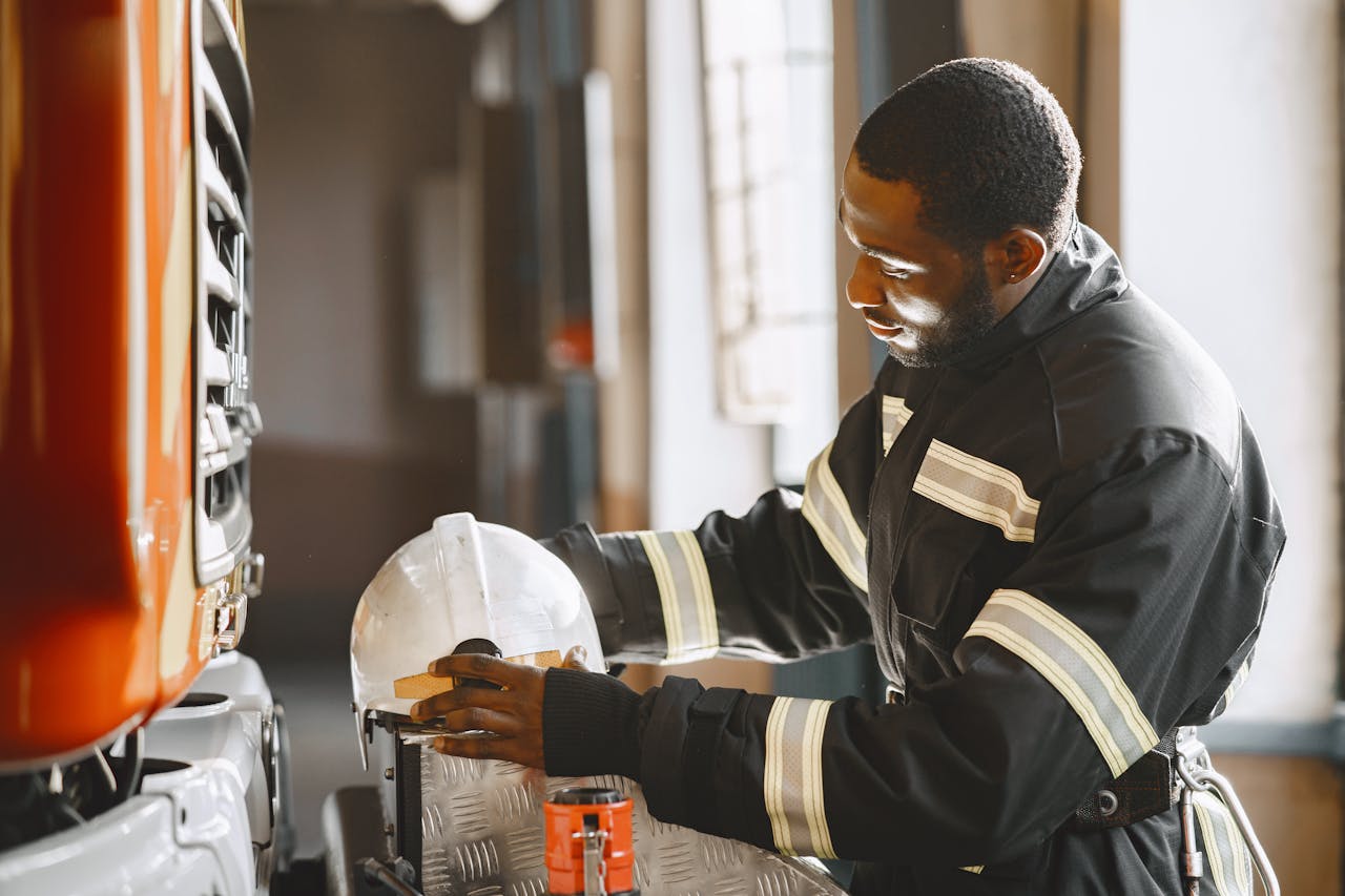 An adult firefighter in uniform organizing equipment inside a fire station.